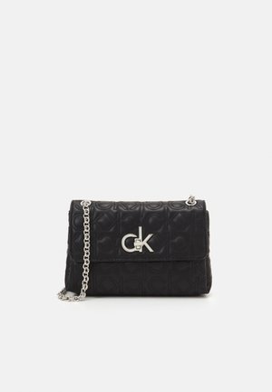 Czarna pikowana skórzana torebka na ramię z srebrnym logo Calvin Klein i łańcuszkowym paskiem na jednolitym tle.