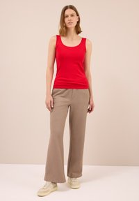 Top senza maniche rosso abbinato a pantaloni a gamba larga marrone chiaro. L'outfit presenta un tessuto morbido e una vestibilità rilassata. Sneakers casual completano il look.