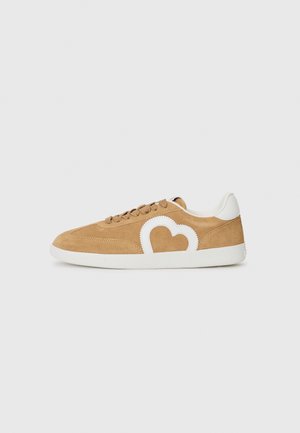 Tan semskinn sneakers med hvit hjerteformet design, rund tå, tonede snørebånd og hvit gummisåle. Jevnt stoff kontrasterer med den myke overflaten.