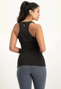 Schwarzes, figurbetontes Tanktop mit Racerback-Design, glatter Textur und dezentem Logodetail auf der Rückseite, kombiniert mit grauen Sportleggings.
