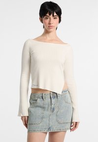 Maglione a coste senza spalle di colore avorio abbinato a una mini gonna in denim chiaro. Il maglione presenta una vestibilità cropped e maniche a sbuffo.
