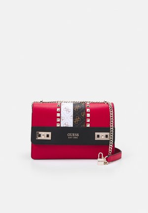 Sac bandoulière Guess rouge et noir avec chaîne, clous dorés, charm en forme de serrure et rayures verticales blanches et noires sur le rabat avant.