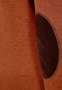 Sweter w kolorze rdzy z prążkowanym wzorem, z ciemnobrązową zamszową łataną na łokciu oraz kontrastowym przeszyciem na brzegach.