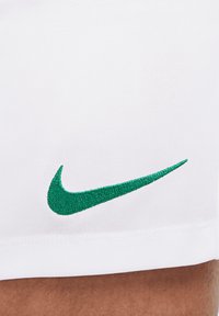 Shorts de sport blancs avec un logo Nike swoosh brodé vert, fabriqués en tissu respirant avec une surface texturée.