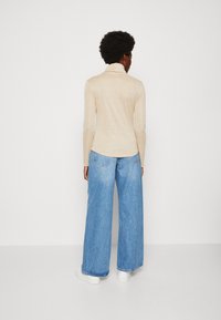 Beige langekous top met een kraag; gecombineerd met brede blauwe denim jeans en witte sneakers. De top heeft een subtiele glans.