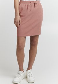 Rosa, ribbet strikket skjørt med snøring i midjen, med sidelommer og en tettsittende design, kombinert med hvite sneakers.