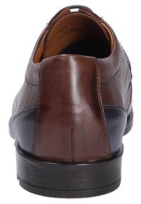Brown leather shoe with a dark blue accent, smooth texture, rounded shape, and a low black sole. Features stitching details on the sides.