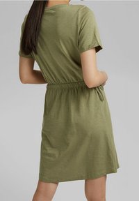 Robe vert olive à manches courtes avec une coupe décontractée, taille élastique et détail à nouer. Tissu doux et léger avec une texture lisse.