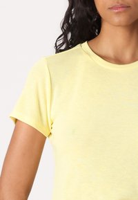 Camiseta amarilla de manga corta con cuello redondo clásico. Confeccionada con una tela suave y ligera que presenta una textura suave y un patrón ligeramente jaspeado.