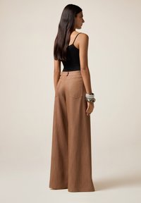 Pantalons larges marron avec une finition texturée, taille haute et poches arrière, associés à un haut noir sans manches et des bracelets en argent.