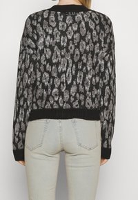 Svart och grå djurmönstrad tröja med ribbat rundhals och nederkant, med en lös passform och långa ärmar, ihop med ljusgrå jeans.