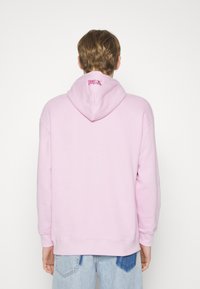 Rozā kapuce ar brīvu piegriezumu, aprīkota ar aukliņu un logo izšūtu mugurpusē. Mīksta auduma un ribotas aproces.