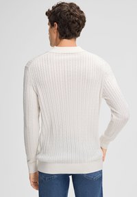 Helle cremefarbene Strickjacke in Kabelstrickoptik mit gerippter Struktur, langen Ärmeln und rundem Kragen. Verfügt über einen figurbetonten Bund und Bündchen.