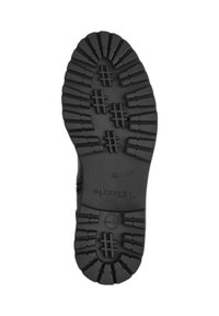Semelle de chaussure en caoutchouc noir avec de profonds rainures et crêtes pour une adhérence, dotée d'un logo circulaire près de l'orteil et d'un nom de marque en relief.
