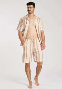 Korte mouwen, geknoopte blouse en bijpassende short in beige met geometrische rode patronen. Lichtgewicht stof, ontspannen pasvorm, drawstring tailleband.