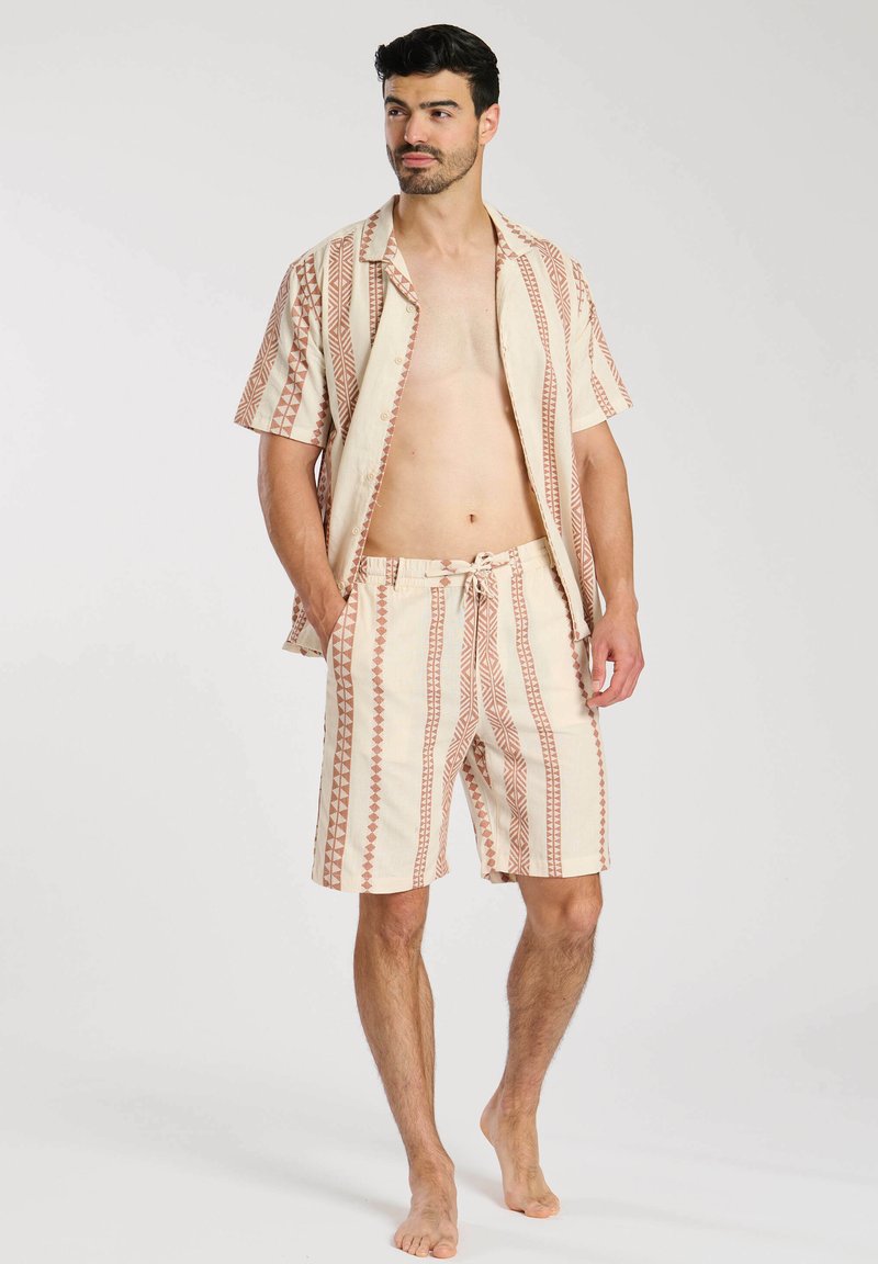 Korte mouwen, geknoopte blouse en bijpassende short in beige met geometrische rode patronen. Lichtgewicht stof, ontspannen pasvorm, drawstring tailleband.