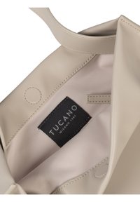 Borsa a tracolla Tucano in morbido materiale beige con texture liscia; include un'etichetta all'interno e una chiusura con dettaglio a bottone a pressione.