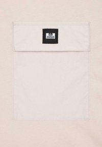 Jasnokremowa tkaninowa kieszeń z klapką, z małą czarną metką z napisem "Weekend Offender" w białym kolorze.