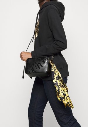 Borsa a tracolla in pelle nera con logo impresso, forma rettangolare, frangia laterale, accentuata da una sciarpa di seta con motivo dorato.