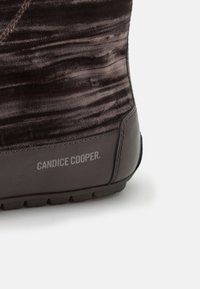 Botte à la cheville brun foncé avec un dessus en velours texturé, des accents en cuir et une semelle en caoutchouc avec un logo de marque visible.