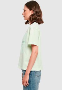Mintgrøn t-shirt, kortærmet, afslappet pasform. Har grafisk motiv foran med tekst og bladmønster. Glat bomuldsstof, rund halsudskæring.