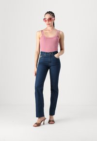 Pink ribbed tank top with lace trim, high-waisted dark blue jeans, and brown heeled sandals. Model wears pink oversized sunglasses.