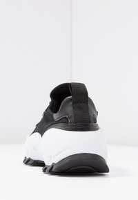 Black athletic shoe featuring a textured upper with leather and fabric, a white midsole, and a pull tab at the heel for easy wear.