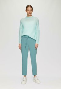 Licht turquoise oversized trui met een hoge halslijn, gecombineerd met strakke teal broeken en witte platform sneakers. Eenvoudig ontwerp en materialen.