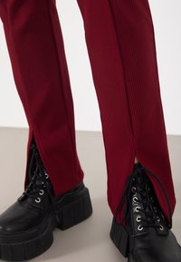Burgundy ribbed pants with side slits, paired with black platform lace-up boots featuring metal eyelets and thick soles.