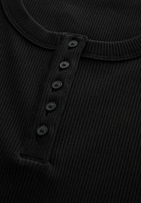 Sort ribbet stof henley skjorte med rund halsudskæring og fem sorte knapper forneden. Glat tekstur, tætsiddende design.