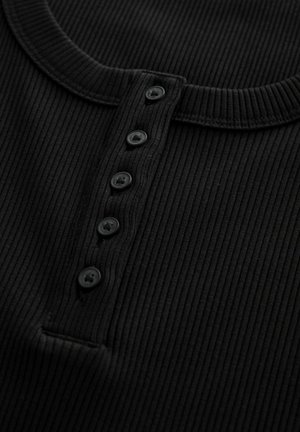 Chemise henley en tissu côtelé noir avec un col rond et cinq boutons noirs sur le devant. Texture lisse, design ajusté.
