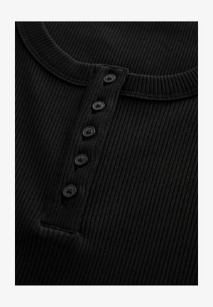 Chemise henley en tissu côtelé noir avec un col rond et cinq boutons noirs sur le devant. Texture lisse, design ajusté.