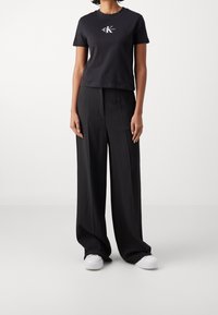 Camiseta corta negra con detalle de logo, combinada con pantalones negros de pierna ancha de cintura alta y zapatillas blancas. Textura de algodón suave.