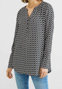 Černobílá halenka s dlouhými rukávy, výstřihem do V, s kruhovým vzorem a knoflíky vpředu, vyrobená z lehkého materiálu.
