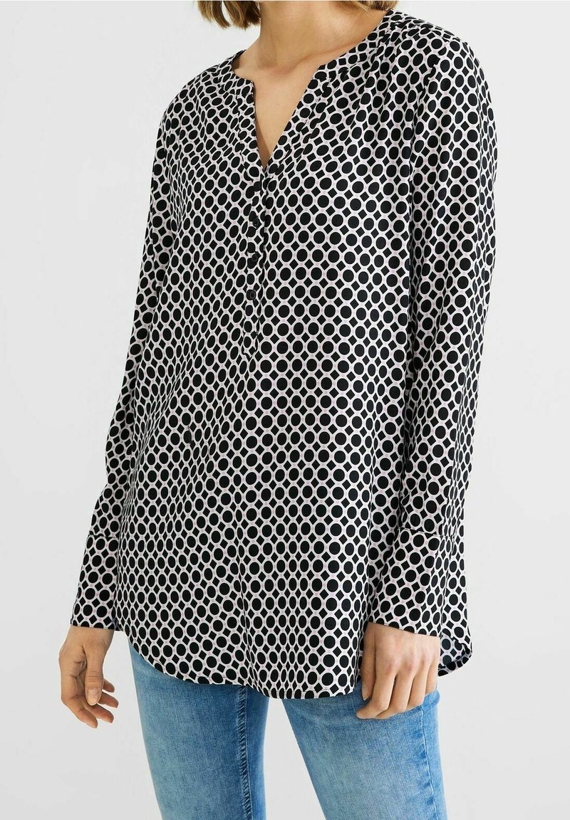 Černobílá halenka s dlouhými rukávy, výstřihem do V, s kruhovým vzorem a knoflíky vpředu, vyrobená z lehkého materiálu.