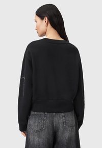 Sweatshirt cropped nero con scollo rotondo e maniche lunghe. Presenta dettagli metallici sulla manica sinistra e una texture morbida.