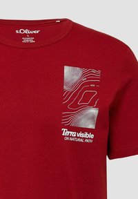 Czerwona koszulka s.Oliver z białą grafiką konturową mapy oraz napisem "Terra visible ON NATURAL PATH" na lewej piersi.