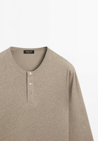 T-shirt Henley beige à manches longues avec trois boutons et col rond, en tissu doux, étiquette indiquant Massimo Dutti.