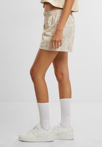 Beige gemusterte Shorts mit elastischem Bund und seitlichen Taschen, kombiniert mit weißen Sneakern und knielangen Socken.