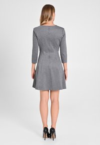 Graues Skaterkleid mit tailliertem Oberteil und schwingendem Rock; hat Dreiviertelärmel und einen Reißverschluss auf der Rückseite. Schwarze High Heels runden das Outfit ab.