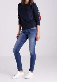 Felpa blu navy con lettering in rilievo, abbinata a jeans skinny azzurri e sneakers bianche. Design semplice, texture morbida.