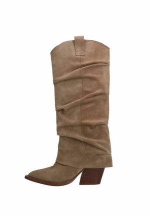 Hohe, beige Wildleder-Cowboy-Boots im Slouchy-Stil mit spitzer Zehenform und gestapeltem Holz-Mid-Heel vor weißem Hintergrund.