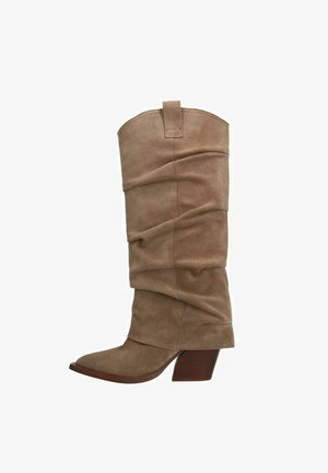 Hohe, beige Wildleder-Cowboy-Boots im Slouchy-Stil mit spitzer Zehenform und gestapeltem Holz-Mid-Heel vor weißem Hintergrund.