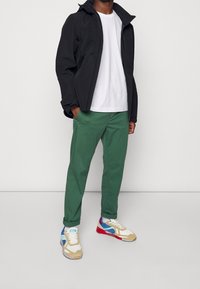 Černá voděodolná bunda, bílá tričko, zelené kalhoty a barevné tenisky s modrými, červenými a béžovými akcenty. Neformální střih a moderní design.