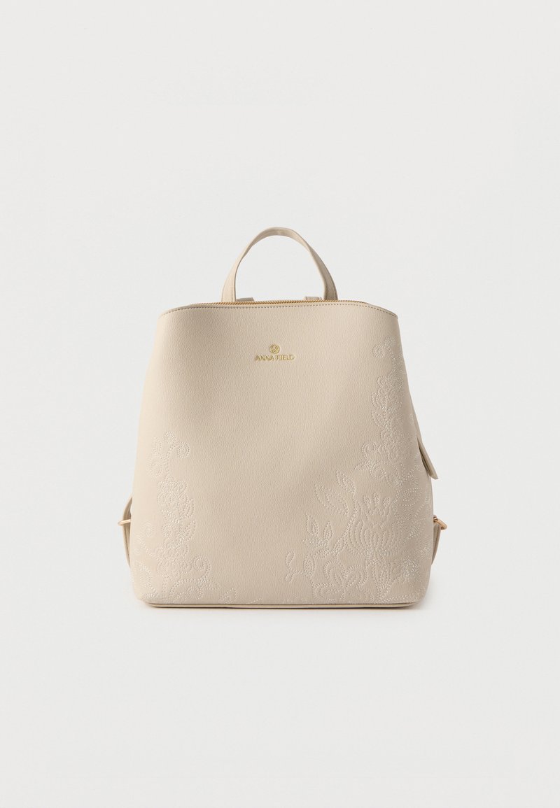 Μπεζ δερμάτινο σακίδιο πλάτης με διακριτική κεντητή ανθική διακόσμηση, πάνω λαβή, ρυθμιζόμενους ιμάντες και χρυσό λογότυπο "Anna Field" στο κέντρο μπροστά.