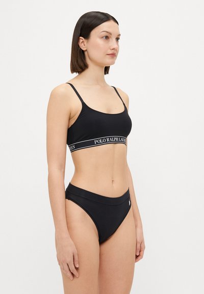 Melnā bikini ar gludu tekstūru. Augšdaļai ir logo lente, bet apakšdaļa ir minimalistiska dizaina ar mazu logo detaļu sānos.