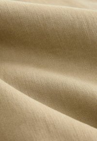 Tan fabric with a smooth, textured surface, featuring diagonal ribbing and subtle sheen. The material is soft and pliable.
