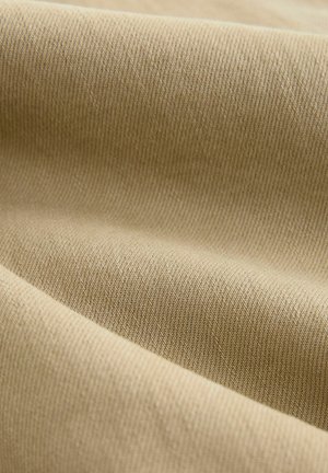 Kreemikas kangas, millel on sile ja tekstureeritud pind, diagonaalsed ribid ja peen sära. Materjal on pehme ja paindlik.