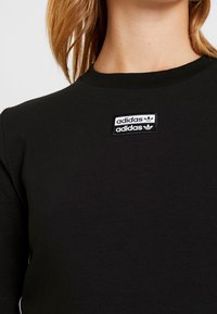 Felpa nera con collo rotondo, caratterizzata da un tessuto testurizzato. Due loghi Adidas bianchi ricamati su una patch rettangolare all'altezza del petto.