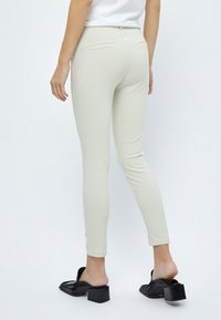 Valkoiset kiinteät housut, joissa on sileä pinta, kahdella takataskulla ja keski korkealla vyötäreellä, yhdistettynä mustiin korkokenkiin.